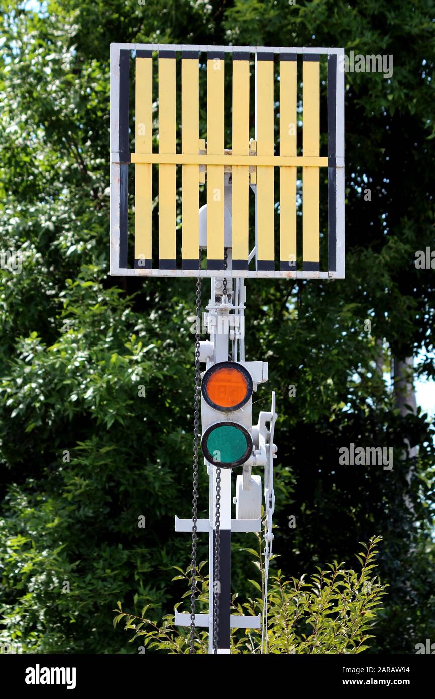 Eisenbahn-Gleisseite rote und grüne Ampel unter dem Signalschild auf Metallstange am örtlichen Bahnhof mit dichten Bäumen im Hintergrund montiert Stockfoto