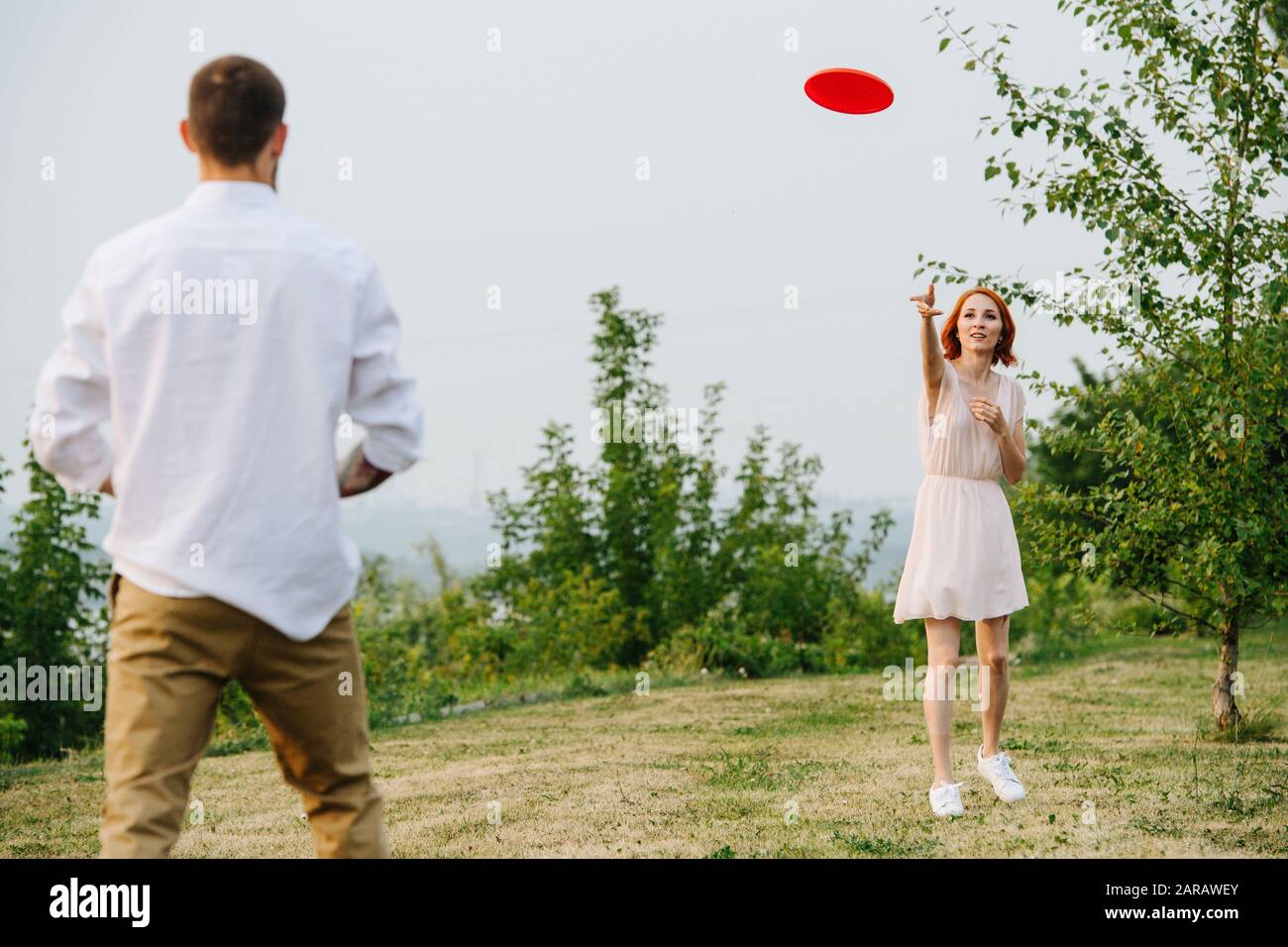 Mann und Frau spielen Frisbee in einem Park neben einem Fluss und einem Waldrücken Stockfoto