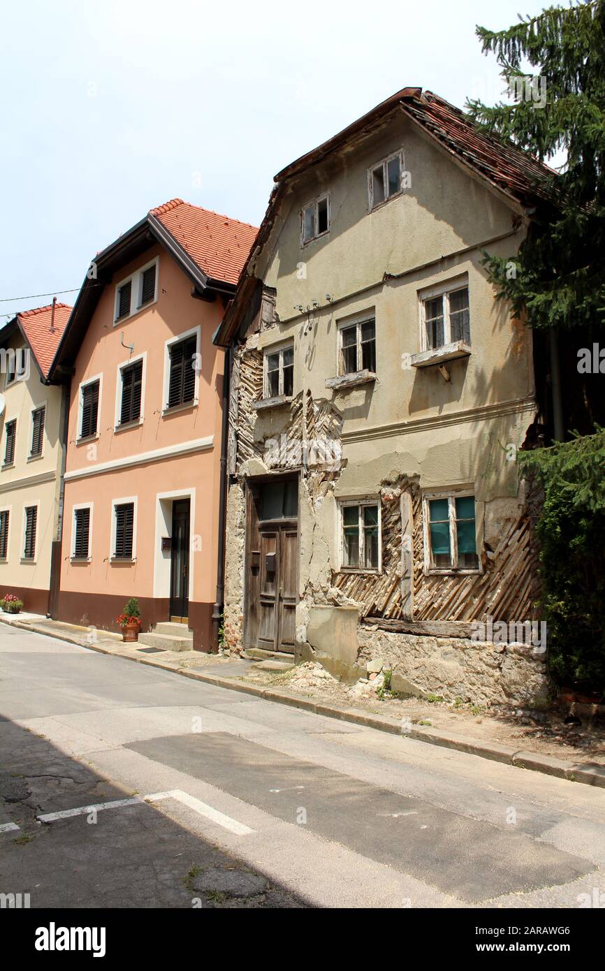 Eine Reihe renovierter, angeschlossener alter Vorstadt-Familienhäuser mit einer verlassenen Ruine am Ende der Straße mit verfallenen, rissenen Wänden und gerissenen Holzbändern Stockfoto