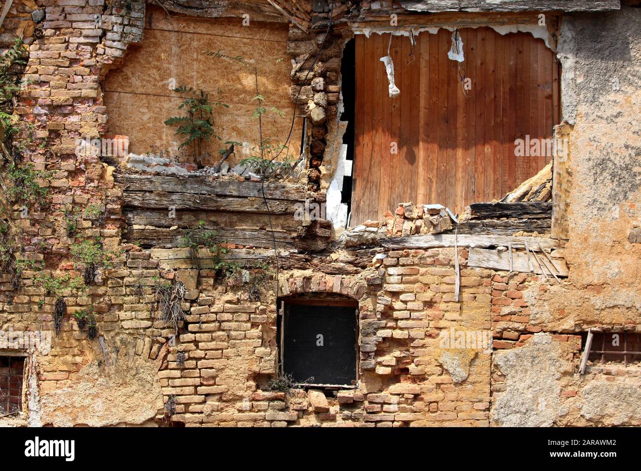 Ruinen des zerstörten alten Hauses aus Holz und roten Ziegelsteinen aus der Vorstadt, gemischt mit kleinen Pflanzen in der Altstadt Stockfoto