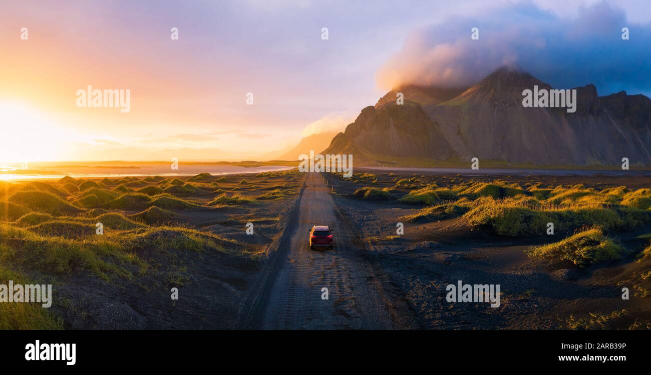 Schotterstraße bei Sonnenuntergang mit Vestrahorn Berg und einem Auto fahren, Island Stockfoto