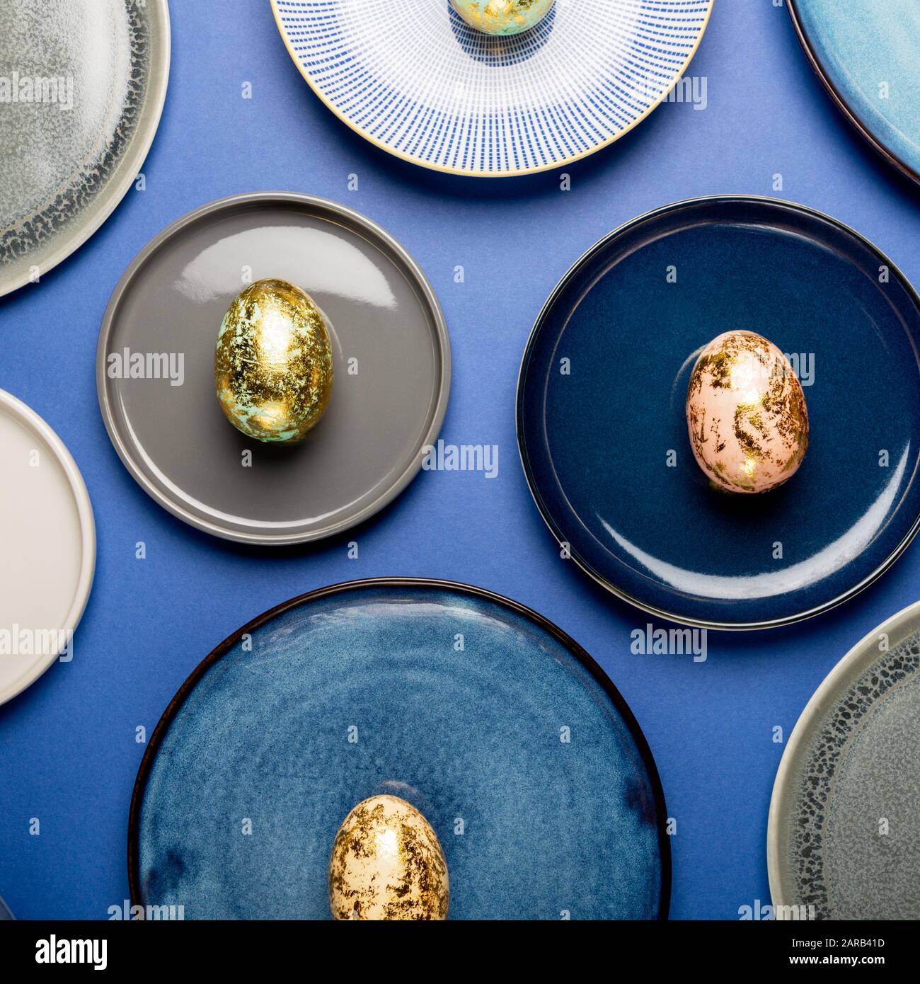 Andere keramische Platten mit goldenen Gesprenkelte Ostereier von Pastellfarben auf blauem Hintergrund. Frohe Ostern Karte Konzept, minimalistisches Design, Ansicht von oben Stockfoto