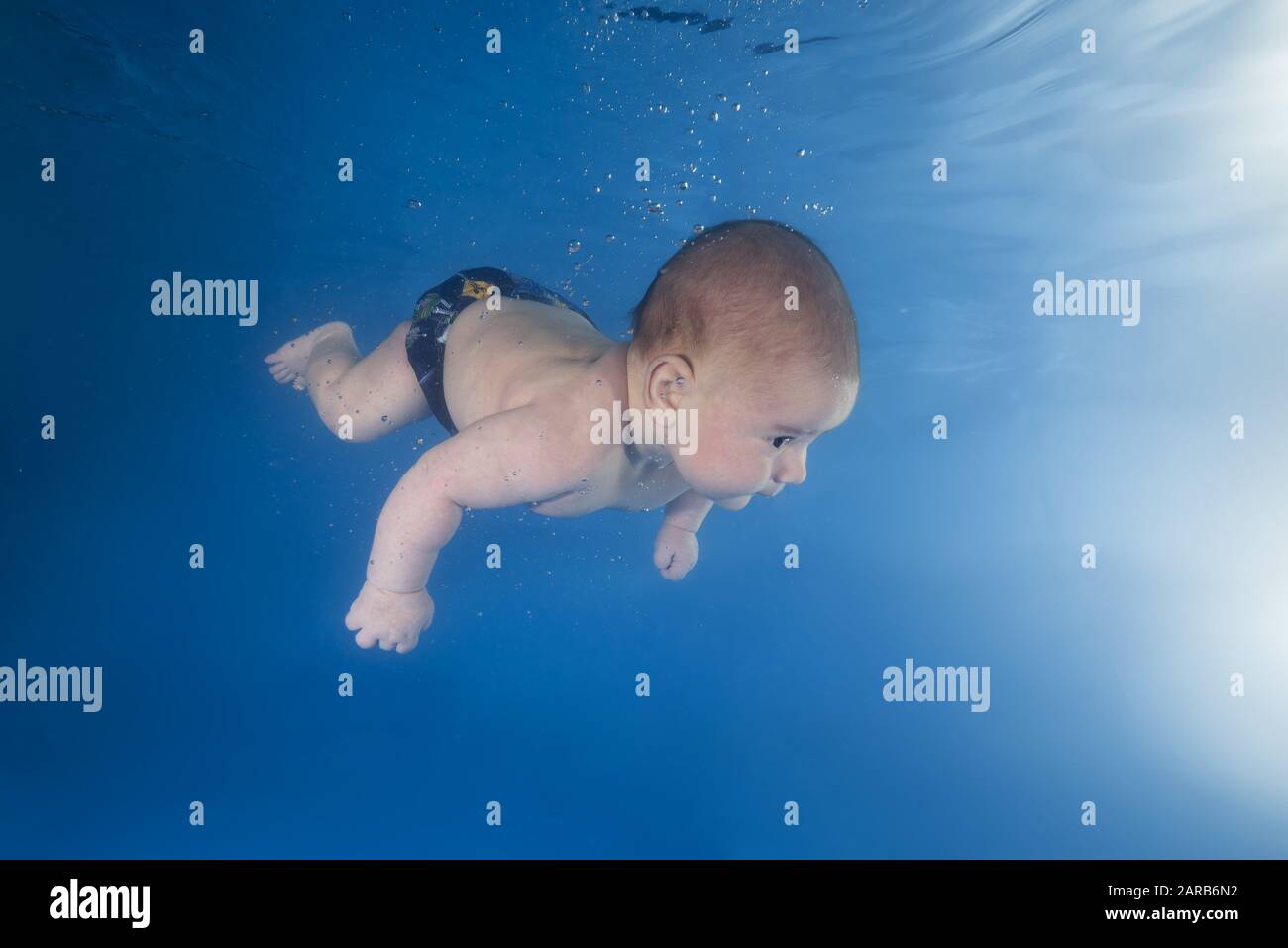 Der kleine Junge lernt, unter Wasser zu schwimmen. Baby schwimmend unter Wasser im Pool auf blauem Wasserhintergrund. Gesunde Familie und Kinder Wasser sp Stockfoto