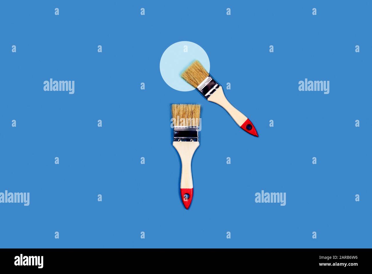 Foto für Wohnungsreparaturen. Blauer Hintergrund mit zwei lackierten Holzquasten und einem Kreis. Flaches Layout, Draufsicht, Kopierbereich. Stockfoto