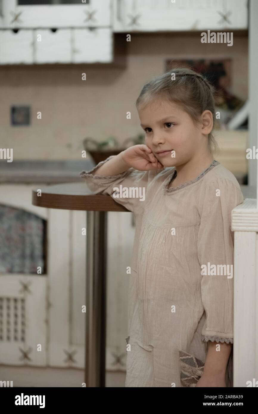 Dunkelblondes Mädchen in beigefarbenem Kleid in der Mitte der Küche. Stockfoto