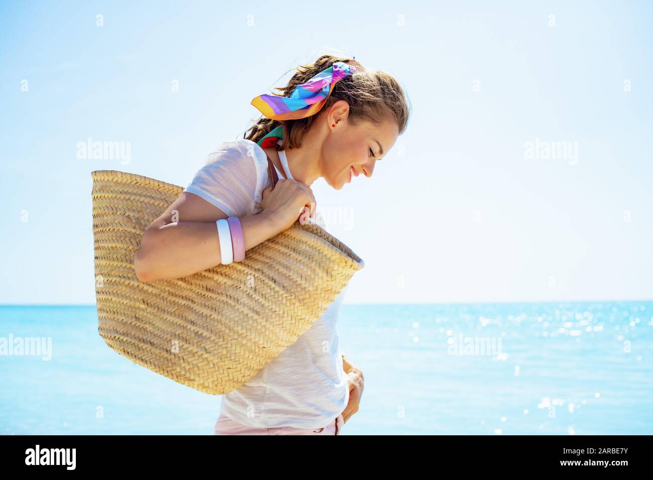 Fröhliche, moderne 40-jährige Frau in weißem T-Shirt mit Strandabschnitt am Strand. Stockfoto