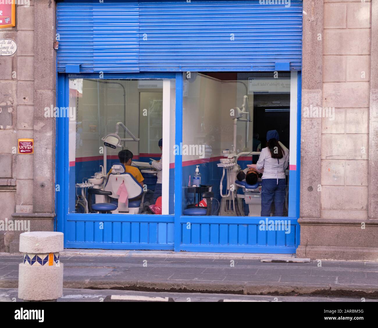 Zahnarztbüro, mit Fenstern, die auf die Straßen geben, wo Passanten den Zahnarzt bei der Arbeit auf einem Patienten im Stuhl sehen können. Puebla, Mexiko Stockfoto