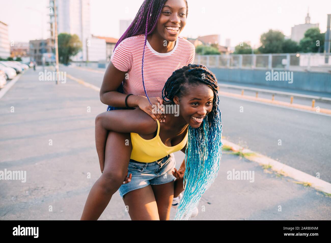 Zwei Schwestern schwarze Frauen im Freien, die Spaß haben, Huckepack zu fahren - Glück, herumtören, Zusammengehörigkeitskonzept Stockfoto
