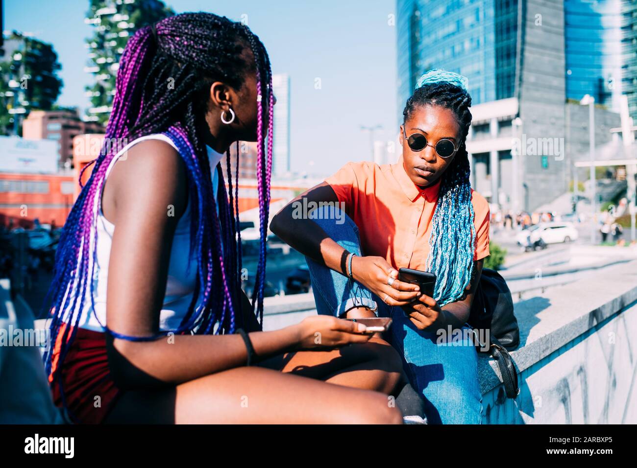 Zwei Schwestern im Freien sitzen im Gespräch und verwenden Smartphone - Phubbing, Isolation, Technologiekonzept Stockfoto