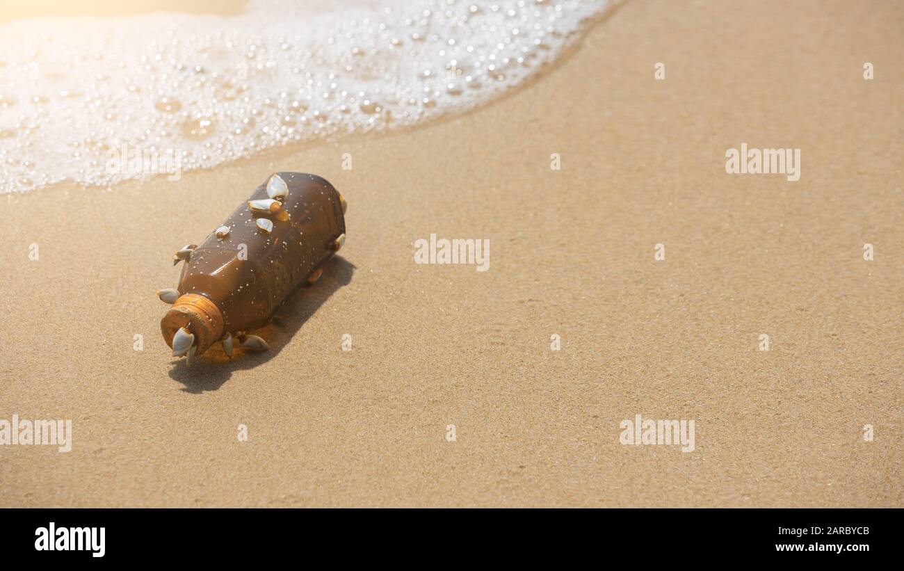 Leere gelbe Glasflasche mit orangefarbenem Deckel wird durch eine Gruppe von Barnacles befestigt. Stück Müll am Strand. Stockfoto