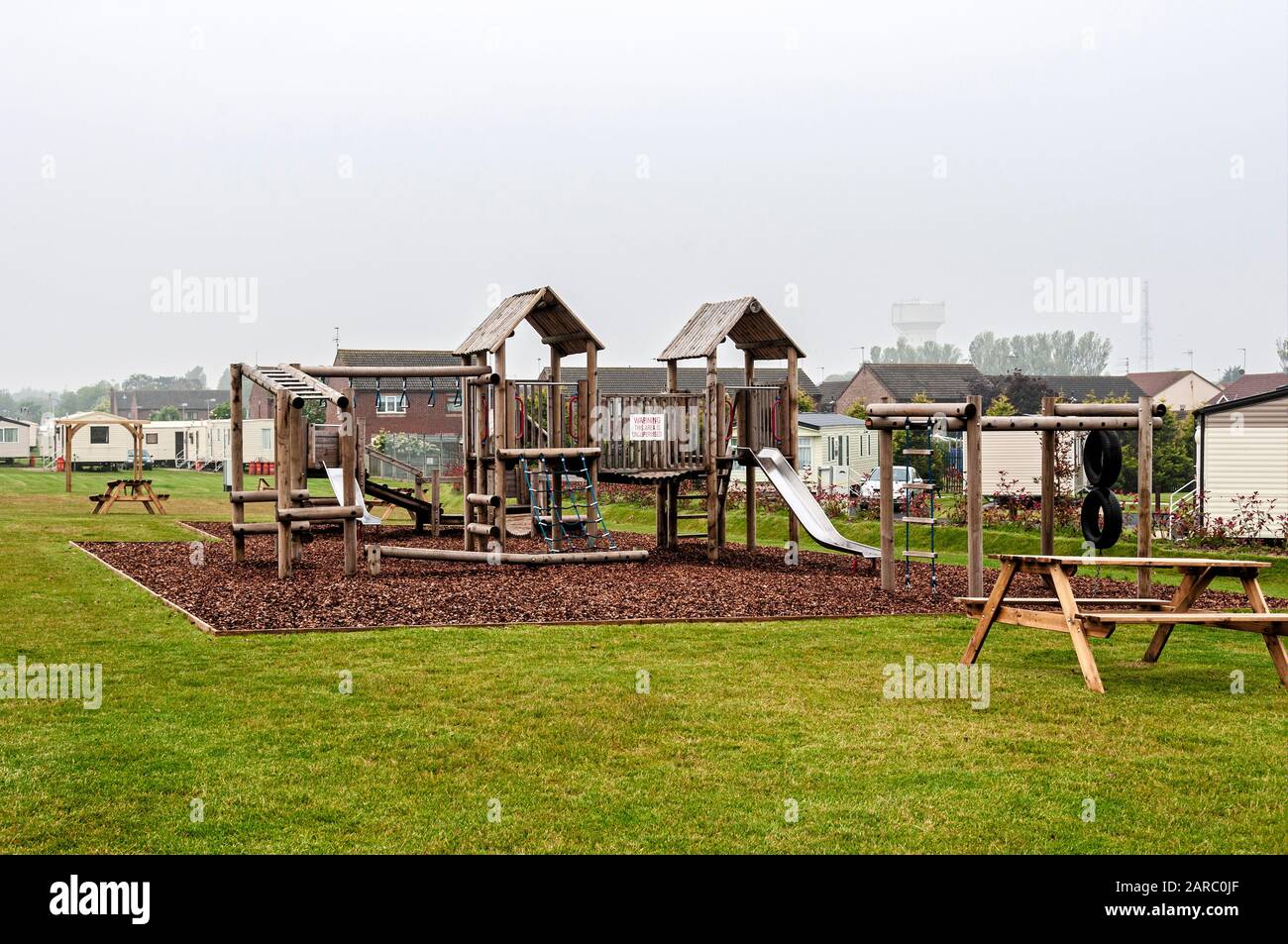 Die Klettergerüste und Objektträger eines Kinderspielbereichs stehen leer auf einer Holzspanfläche unter einem grauen Himmel, da der Meeresnebel die Distanz umhüllt Stockfoto