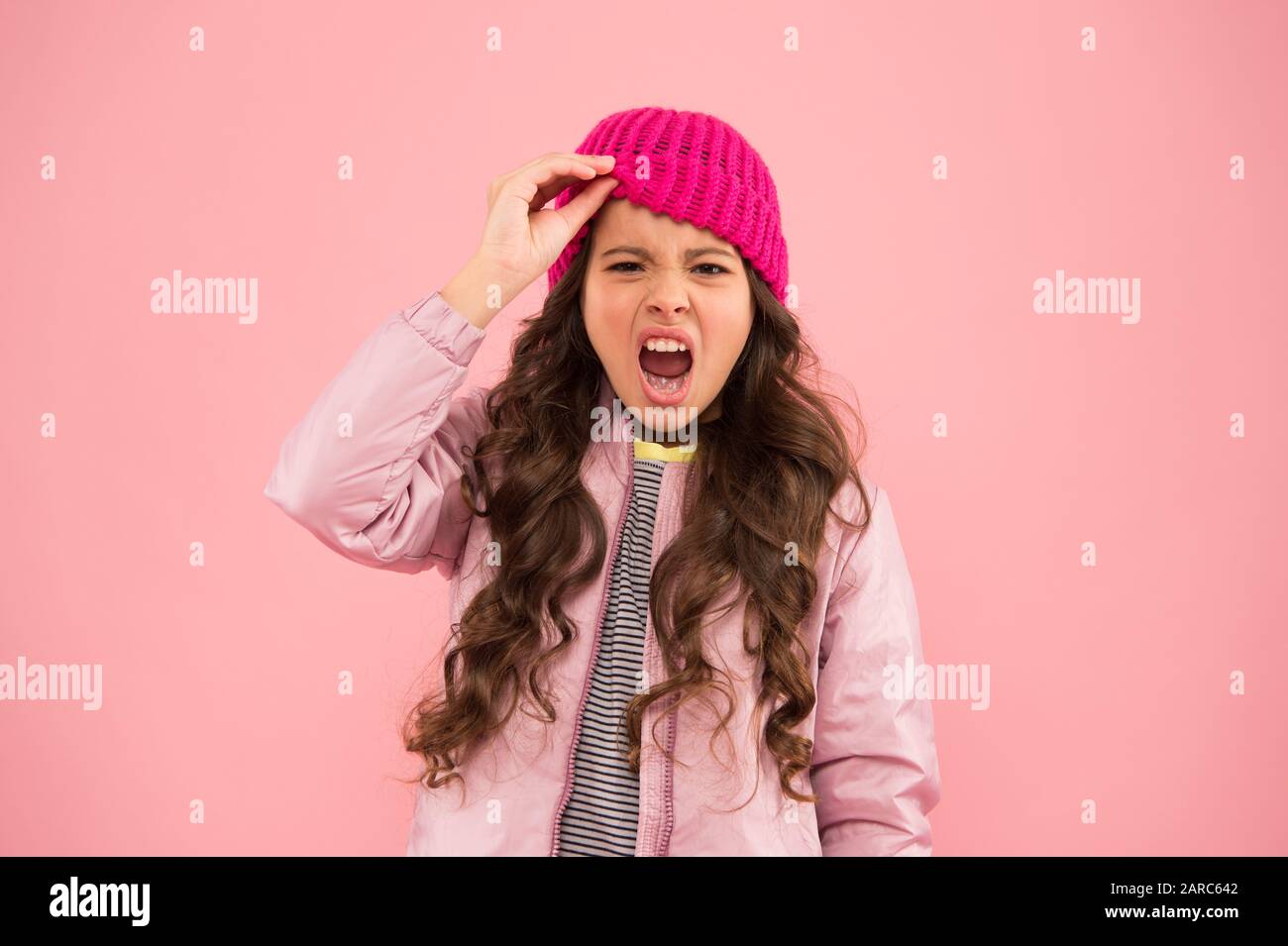 Kleine Mädchen mit pinkfarbenem Hintergrund, Puffer-Jacke und Strickmütze für Kinder, Wintereinkäufe, warme Kleidung im Winter. Mein Lieblingskleidungsartikel. Bereit für den kalten Winter. Kaltes Klima. Stockfoto