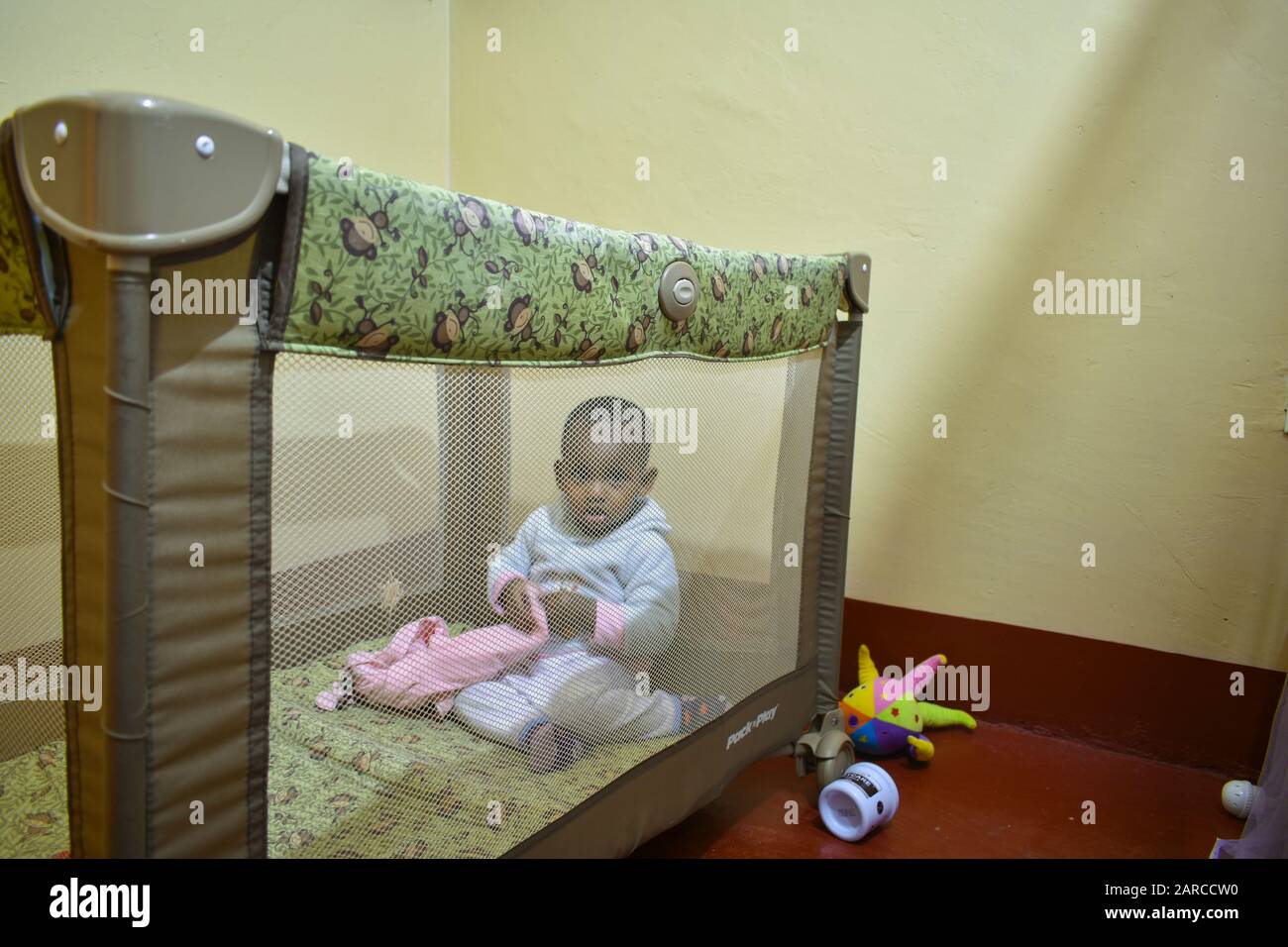 Ein afrikanisches Baby pechelt durch das Netz, während es in einem graco Pack spielt und auf einem Spielplatz spielt. Es ist für Reisen geeignet und kann als Bett dienen Stockfoto