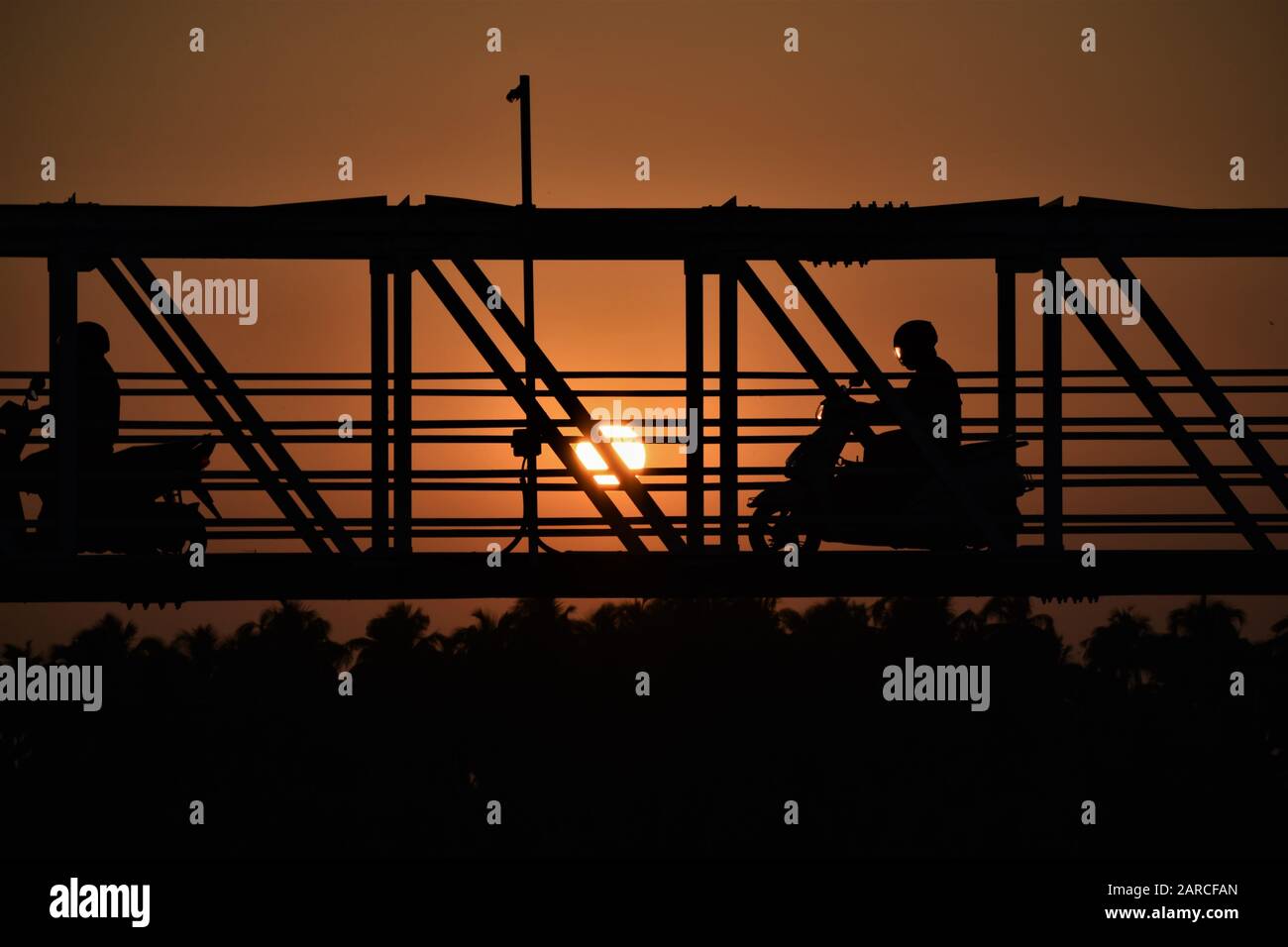 Silhouette einer Brücke in der Abenddämmerung mit schönem Sonnenuntergang und rotem Himmel, Biker in der Brücke Stockfoto