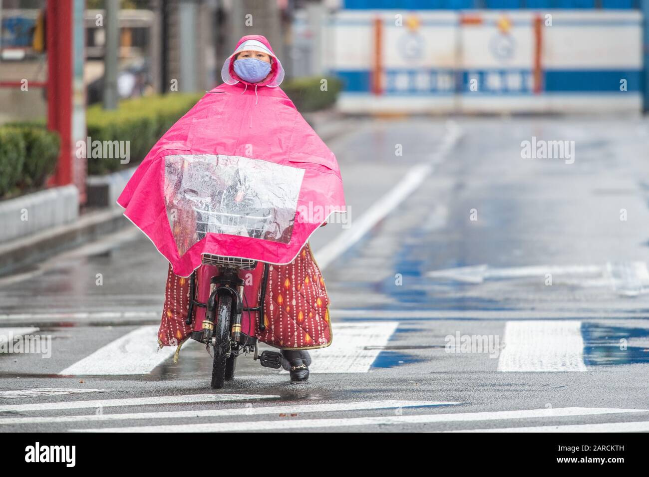Shanghai, China, 25. Januar 2020, EINE Frau, die eine Maske trägt, verwendet Regenponcho, während sie auf der Straße radelt Stockfoto