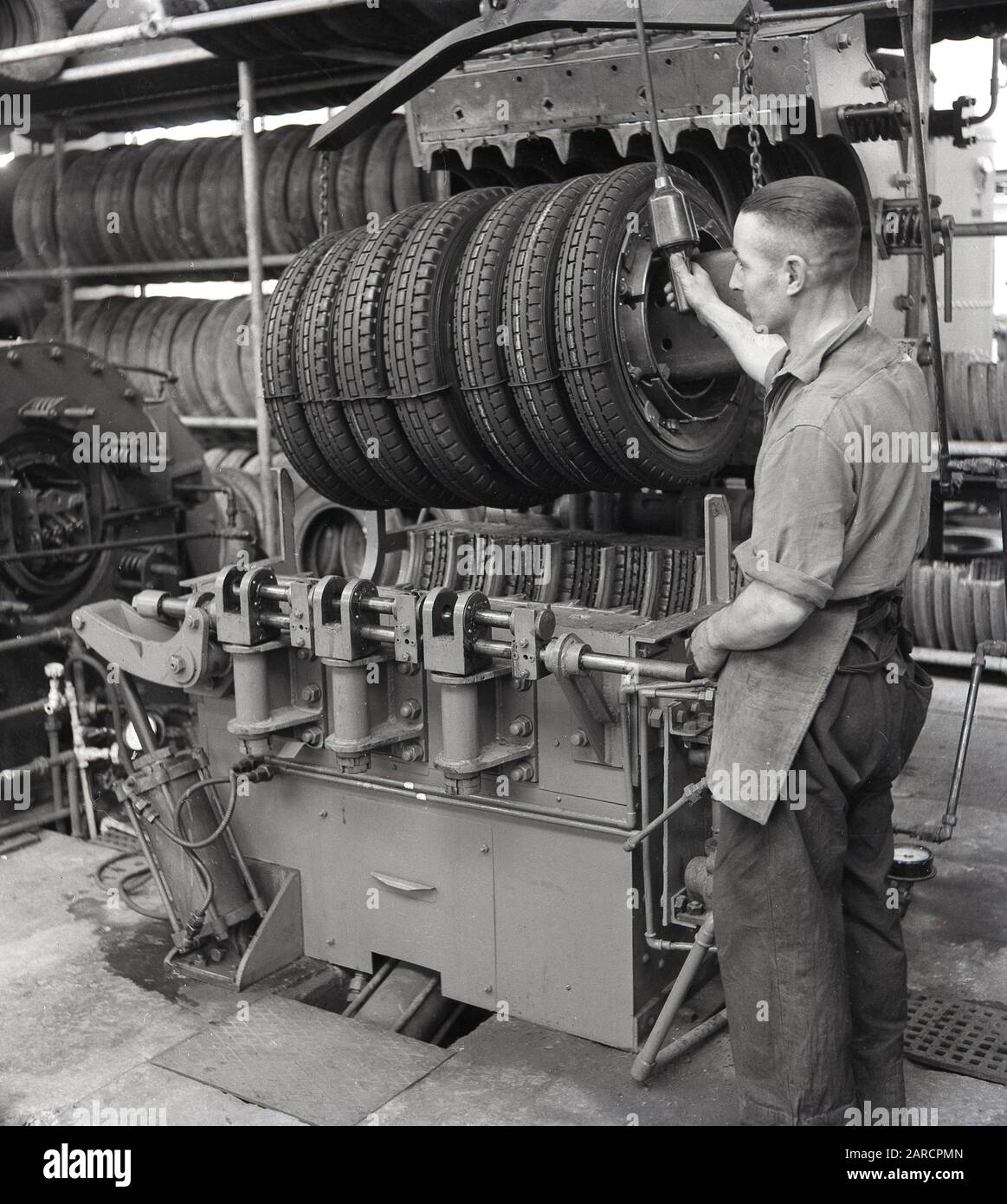 In den 1950er Jahren, historisch, ein Fabrikarbeiter einer neuen Maschine zur Reifenherstellung, eine Aushärtepresse, die den "neuen" Reifen gegen das Laufprofil und die Seitentexte innerhalb der Formen drückte und dem Reifen sein endgültiges Aussehen gab, England, Großbritannien. Stockfoto