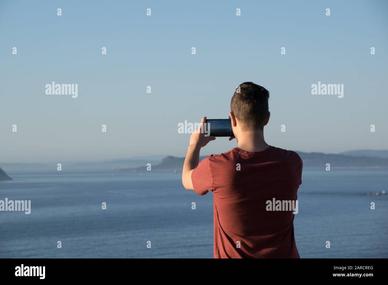 Rückansicht eines Jungen, der ein Foto mit dem Smartphone zum Meer nimmt Stockfoto