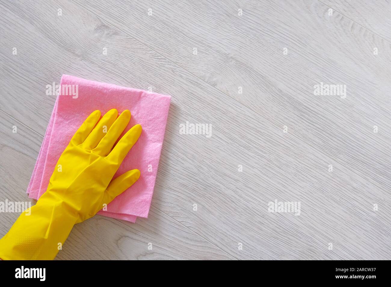 Reinigungskonzept im Büro, zu Hause. Hand in gelbem Gummischutzhandschuh mit Mikrofasertuch reinigen Holzboden. Kopierbereich. Stockfoto