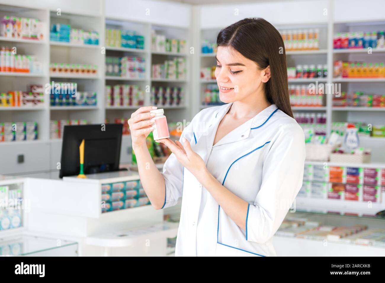 Attraktive Apothekerin mit sanften Händen, die einen kleinen Krug mit Medikamenten oder Vitaminen in einer Apotheke hält Stockfoto