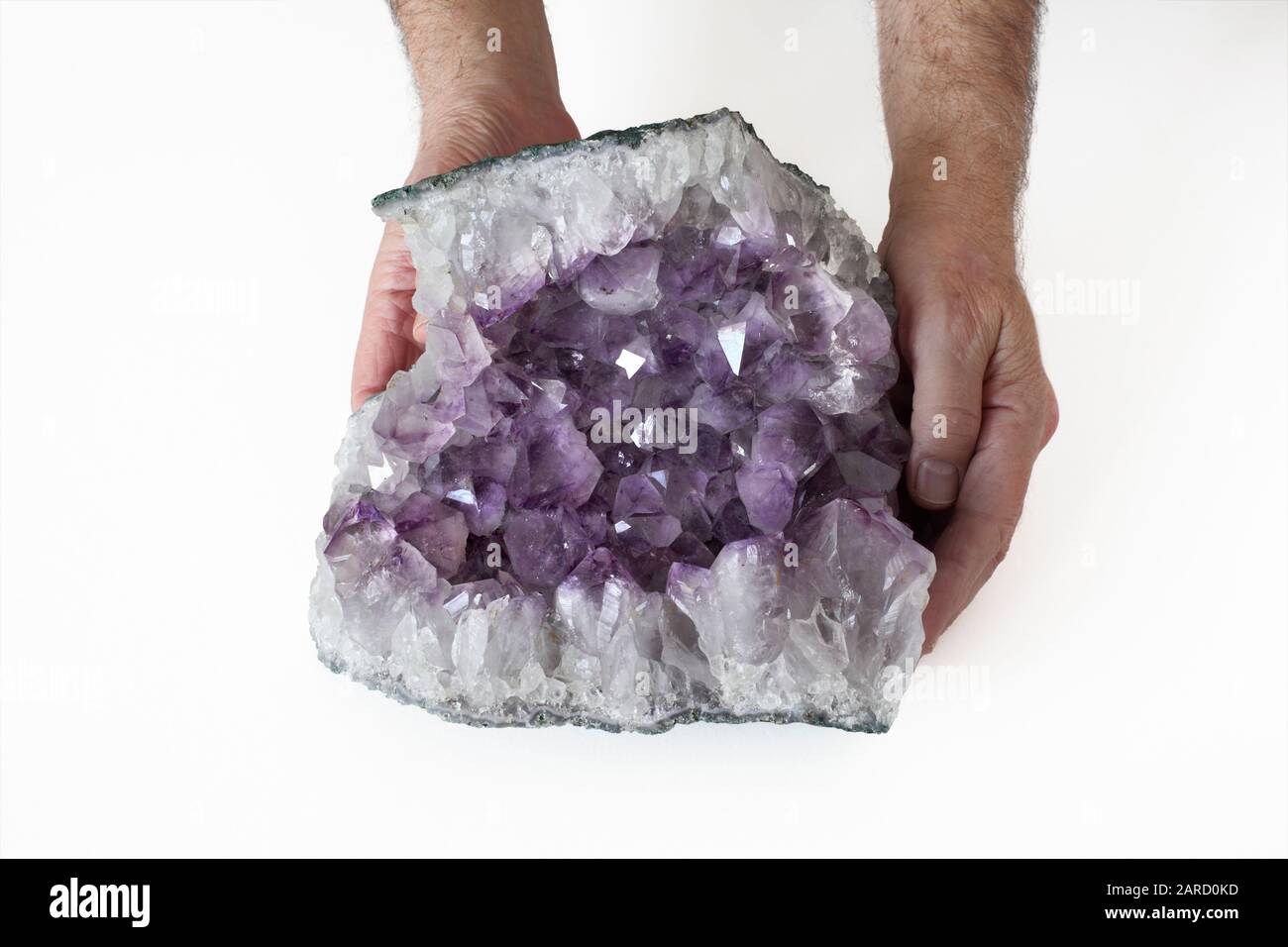 Eine Person, die eine Probe Amethyst hält und die freiliegende Kristallhöhle in einem Felsenabschnitt zeigt. Stockfoto