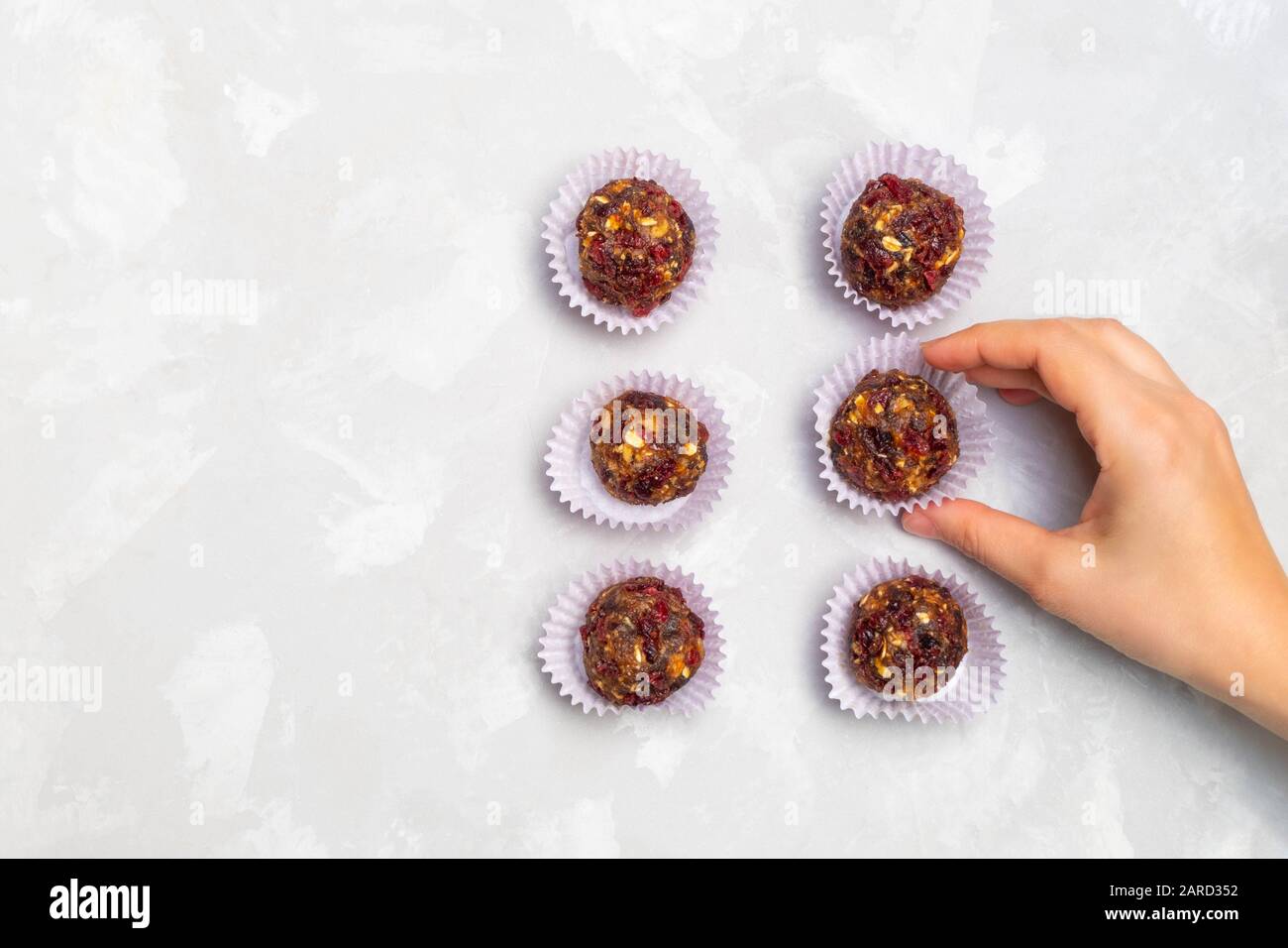 Frau hält vegan rohen Energieball auf neutralem grauem Hintergrund Stockfoto