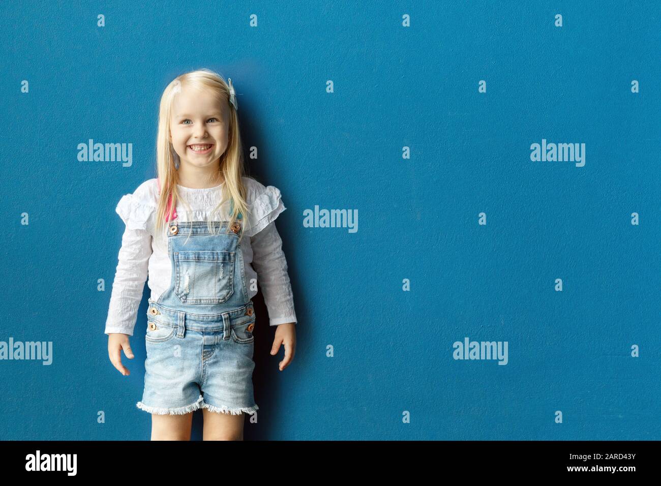 Happy 3-jährige Kleinkind Mädchen lächeln, während posiert gegen blaue Wand Stockfoto