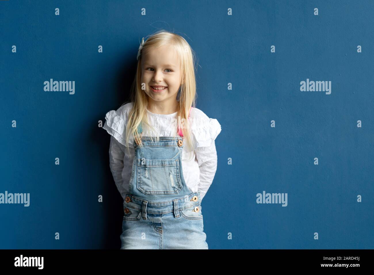 Glücklich Kleinkind hübsches Mädchen lächelnd, während posiert auf blauem Hintergrund Stockfoto