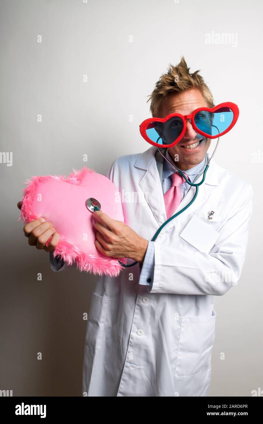 Liebe Doktor mit roten Valentinsgläsern, die auf seinem Stethoskop zu einem großen pinkfarbenen unscharfen Herzen hören Stockfoto