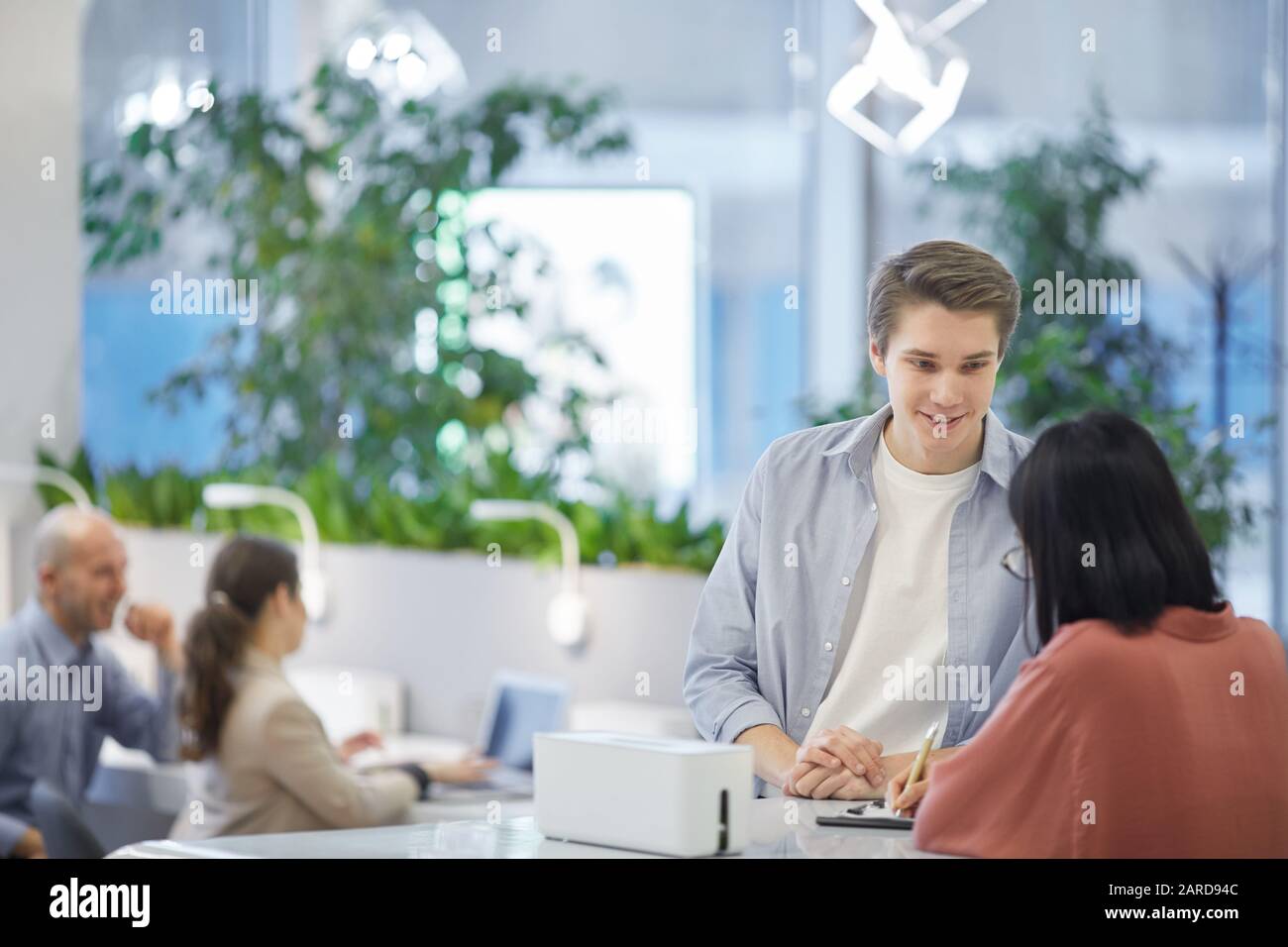Portrait des jungen Mannes, der mit asiatischen Freunden spricht, während er auf einem hohen Schreibtisch steht, Platz für Kopien Stockfoto