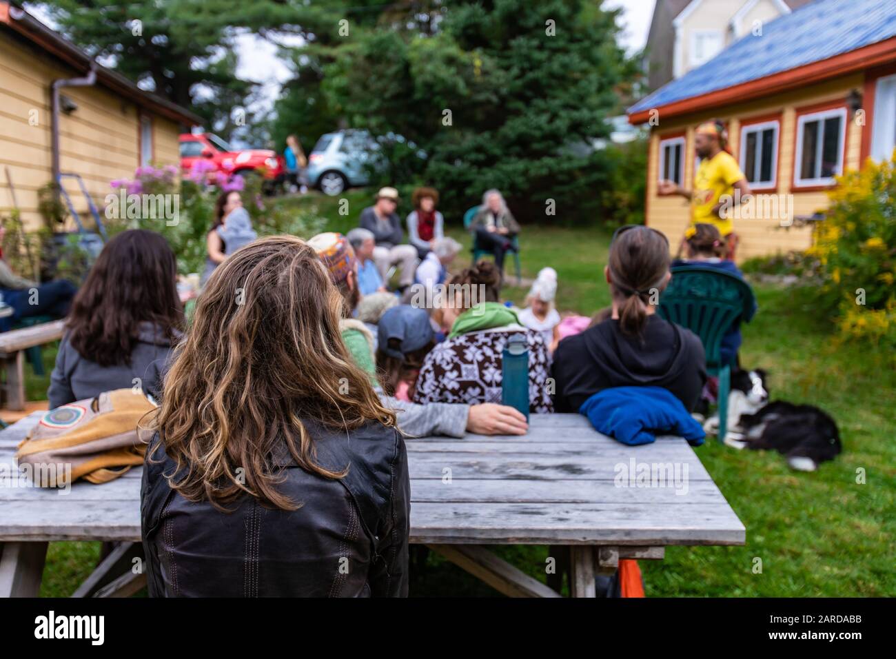 Eine Gruppe von Menschen der mehrstufigen Generation, die während der Veranstaltung im Park gegen Bäume sitzen und sich entspannen, während sie die märchenhafte Geschichte des männlichen Künstlers hören Stockfoto