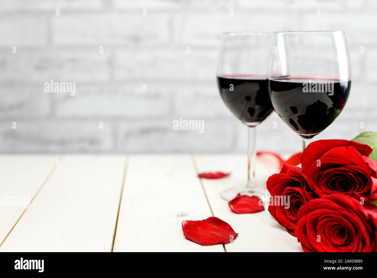 Valentinstag Stillleben. Zwei Gläser Wein, Rosenblätter und rote Rosen auf einem weißen Holztisch mit Platz für Text. Selektiver Fokus. Stockfoto