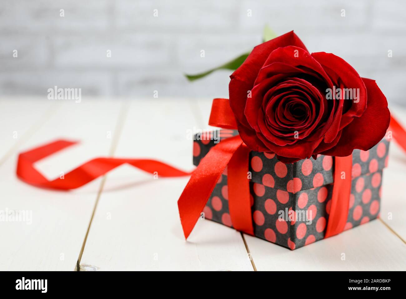 Rote Rose und Geschenkbox auf weißem Holztisch mit Platz für Text. Valentinstag und Muttertagskartenkonzept. Stockfoto