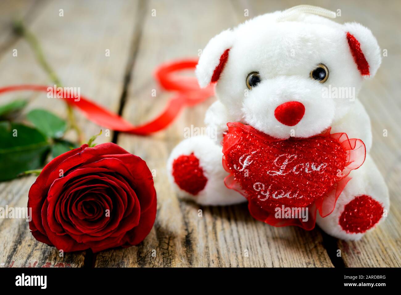 Valentines Tageskonzept. Weißer Plüschspielzeugbär und rote Rose auf Holztisch. Selektiver Fokus. Stockfoto