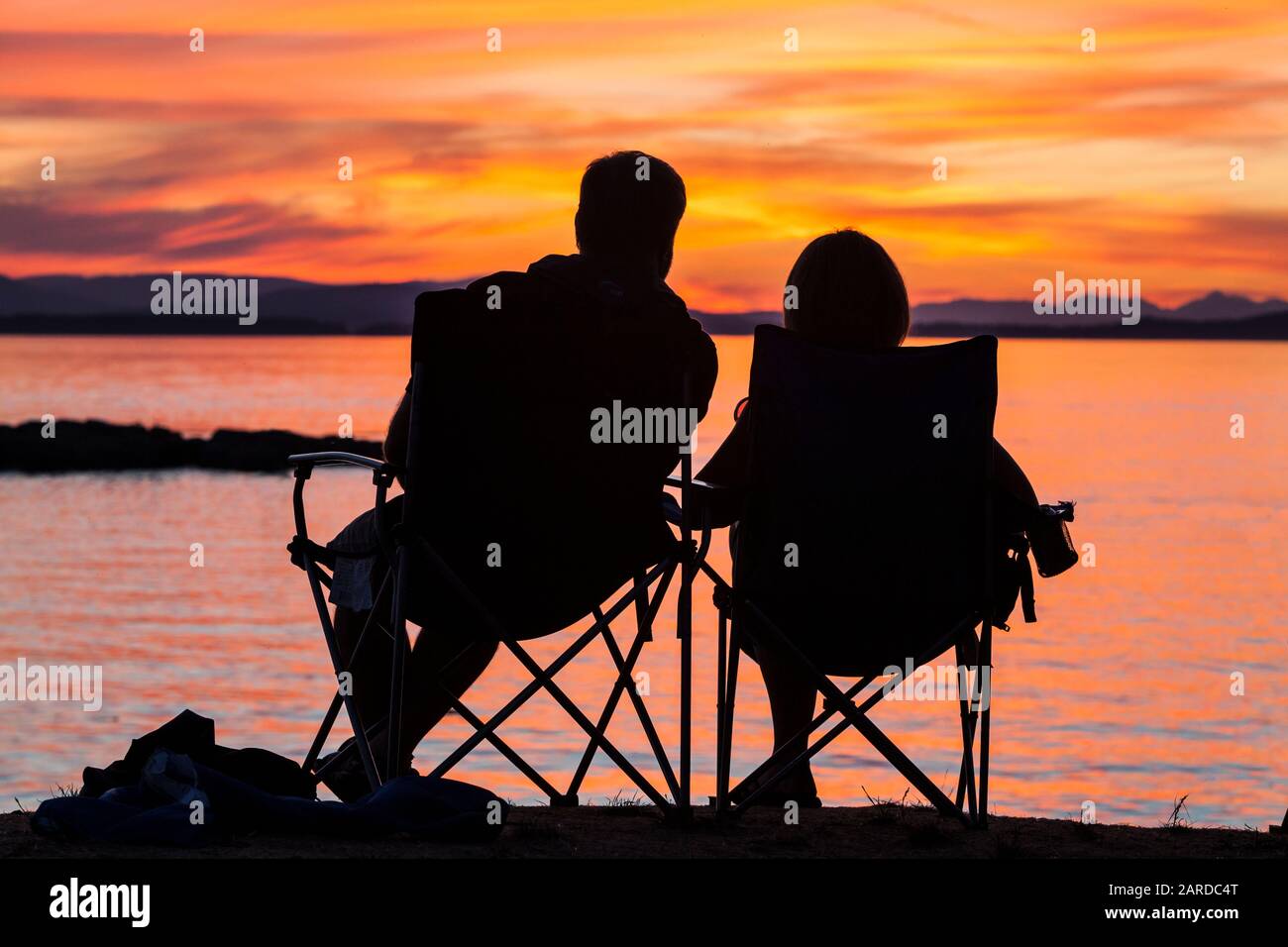 Ein Paar sitzt und beobachtet den Sonnenuntergang über Vancouver Island und Haro Strait, wie es vom County Park auf San Juan Island, Washington, USA, aus gesehen wird. Stockfoto