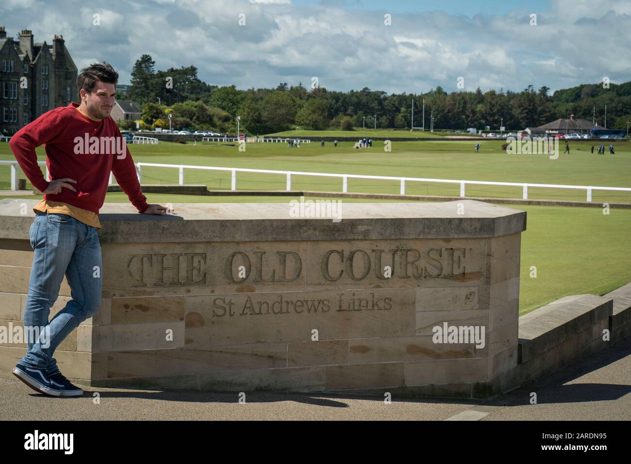 St. Andrews, Großbritannien - 20. Juni 2019: Ein gutaussehender männlicher Tourist lehnt sich an das Schild auf dem Alten Platz im Royal and Ancient Golf Club von St. Andr an Stockfoto