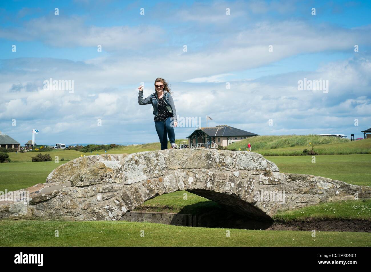 ST Andrews, Großbritannien - 20. Juni 2019: Eine lächelnde Frau hält einen Golfball, während sie auf der Wahrzeichen der Swilcan Bridge am 18. Loch steht Stockfoto
