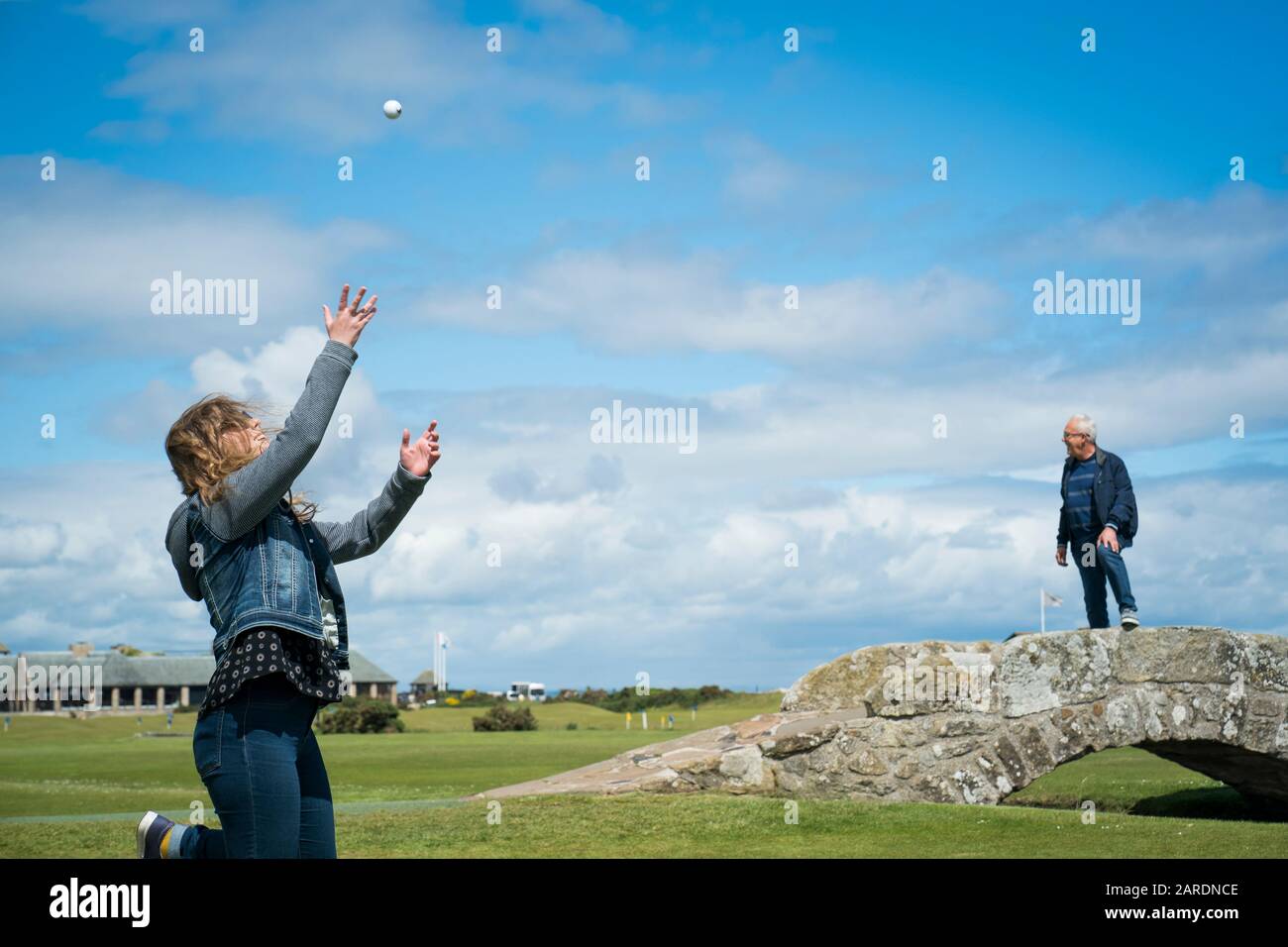 ST Andrews, Großbritannien - 20. Juni 2019: Eine glückliche junge Frau wirft einen Golfball auf, während ein Mann auf der Wahrzeichen von Swilcan Bridge an der steht Stockfoto