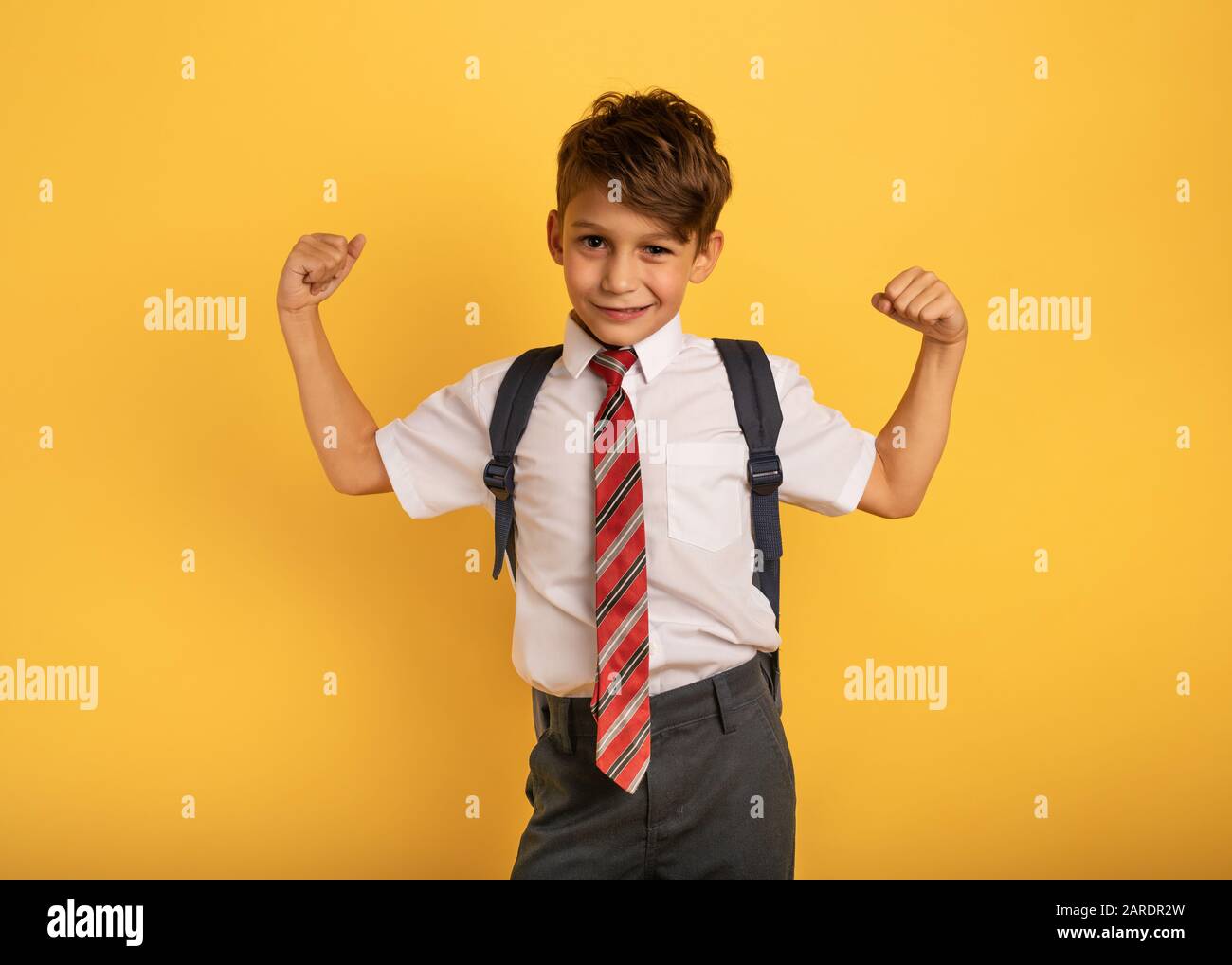 Junge Schüler wirkt wie ein muskulöser Mann. Gelber Hintergrund Stockfoto