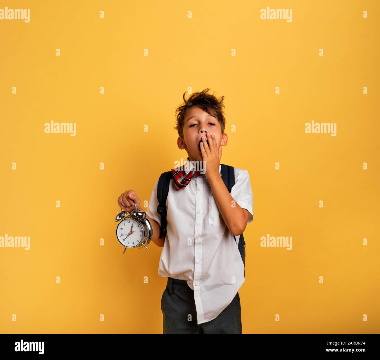 Junge Kind student mit klingelnden Wecker ist faul in die Schule zu gehen. Gelber Hintergrund. Stockfoto