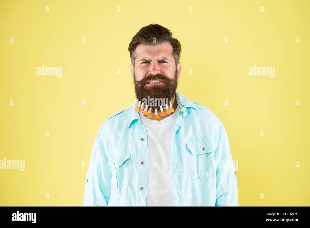 Es tut so weh. Individuelle Frisur für Männer. Man bekleidet sich mit Bart. Brutaler Hüpfer mit Wäschehegen. Bärtiger Mann legerer gelber Hintergrund. Valentinstag. Haartrocknung im Friseur. Stockfoto