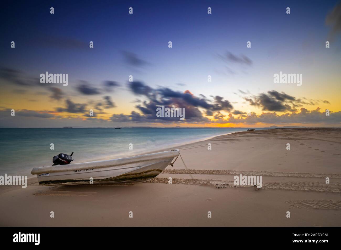 Kleines Dingy mit Außenbordmotor am Strand bei Sonnenuntergang Stockfoto