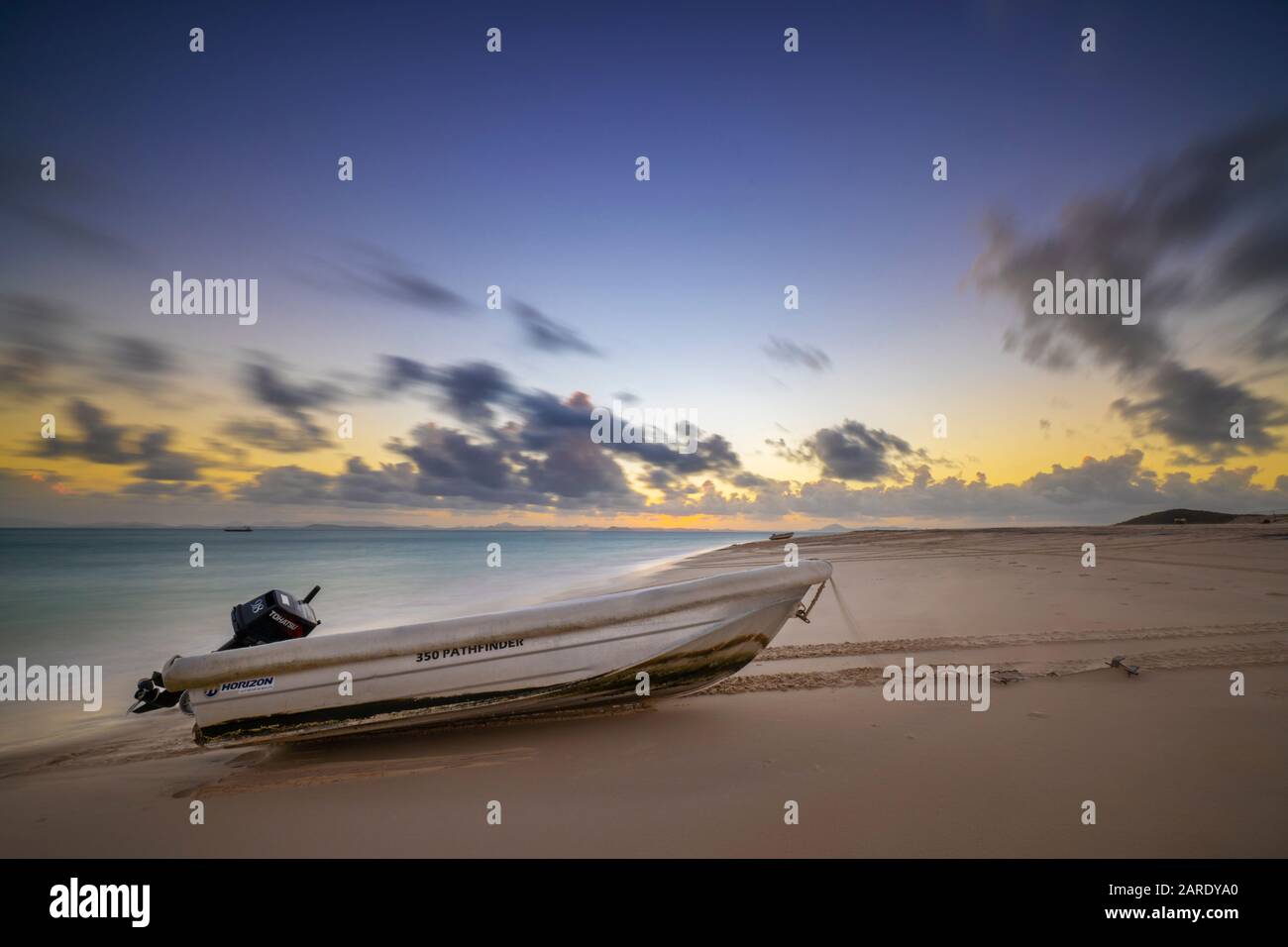 Kleines Dingy mit Außenbordmotor am Strand bei Sonnenuntergang Stockfoto