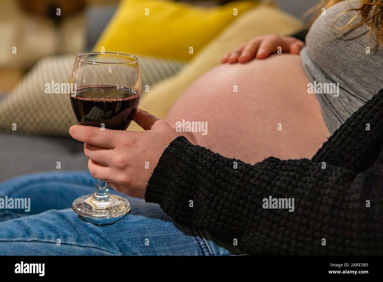 Nahaufnahme und Seitenansicht einer stark schwangeren Frau mit einem Glas Rotwein in der Hand. Alkohol kann dem ungeborenen Baby schaden Stockfoto