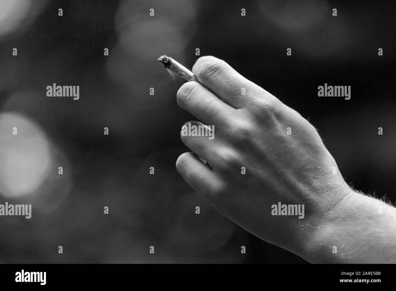 Schwarzweiß-selektiver Fokus-Nahaufnahme von der Hand der kaukasischen Frau, die Marihuana-Gelenk hält. Cannabiszigarette wird außerhalb des Fokushintergrunds geraucht. Stockfoto