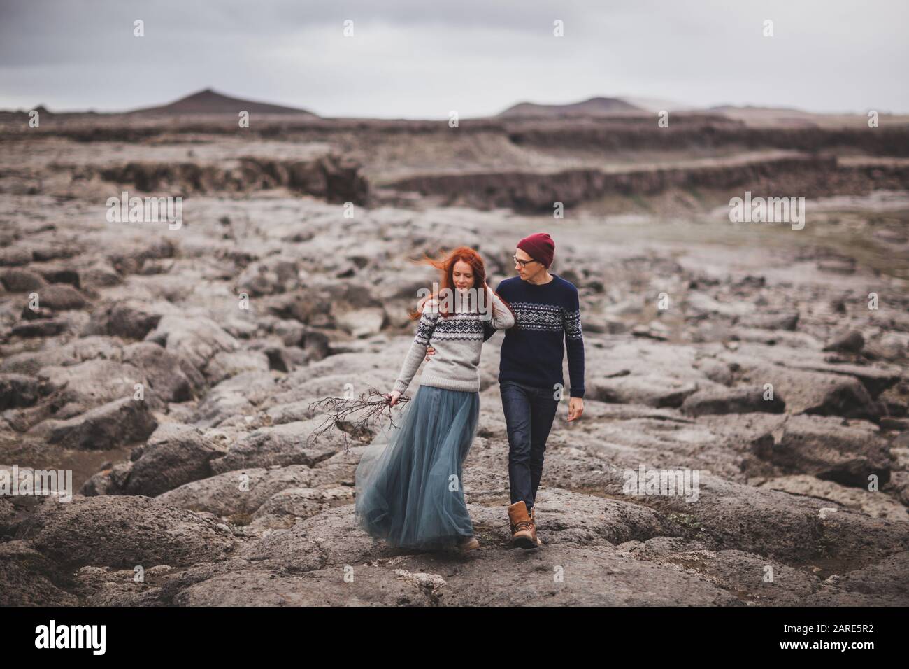 Paar in der Liebe wandern in Island. Stein vulkanischen Wüste herum, in der Mitte von Nirgendwo. Dramatische nordischen Landschaft, bei kaltem Wetter. Das Tragen der traditionellen wolle Pullover, Jeans und Grauer Rock. Stockfoto