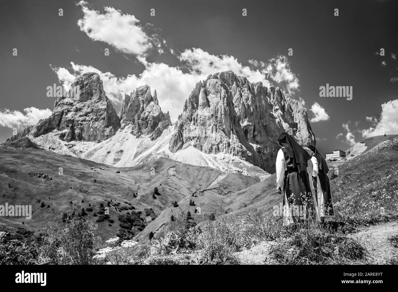 Graustufenaufnahme von Nonnen, die mit Bergen den Hügel hinunter gehen Im Hintergrund Stockfoto