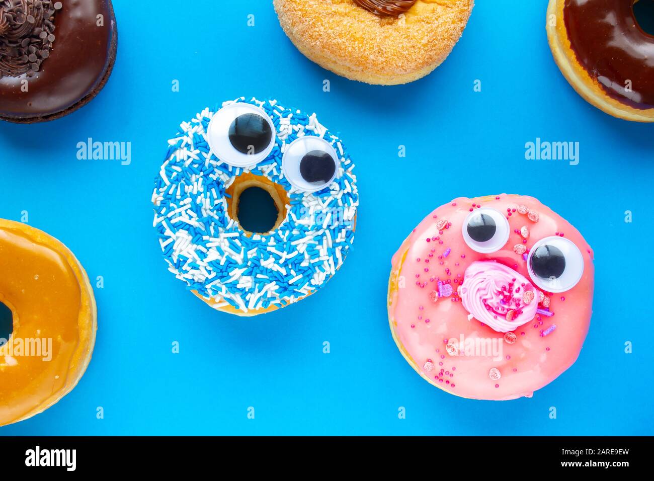 Ein blauer Donut mit einem pinkfarbenen Donut mit lustigen Gesichtern auf blauem Hintergrund, die sich gegenseitig sehen Stockfoto