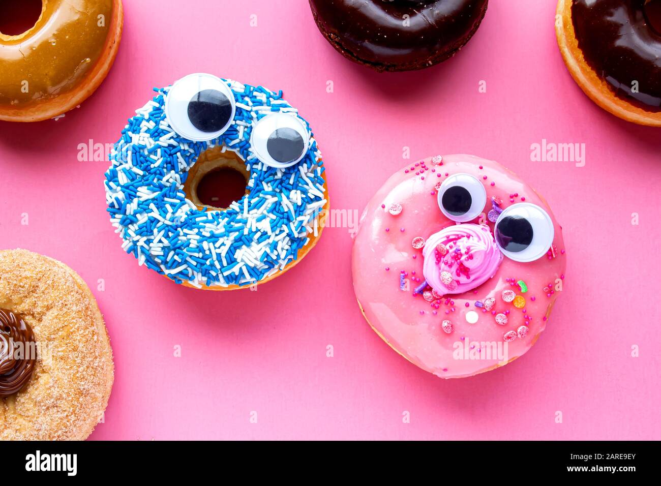 Ein blauer Donut mit einem pinkfarbenen Donut mit lustigen Gesichtern auf einem rosafarbenen Hintergrund, der sich gegenseitig sieht Stockfoto