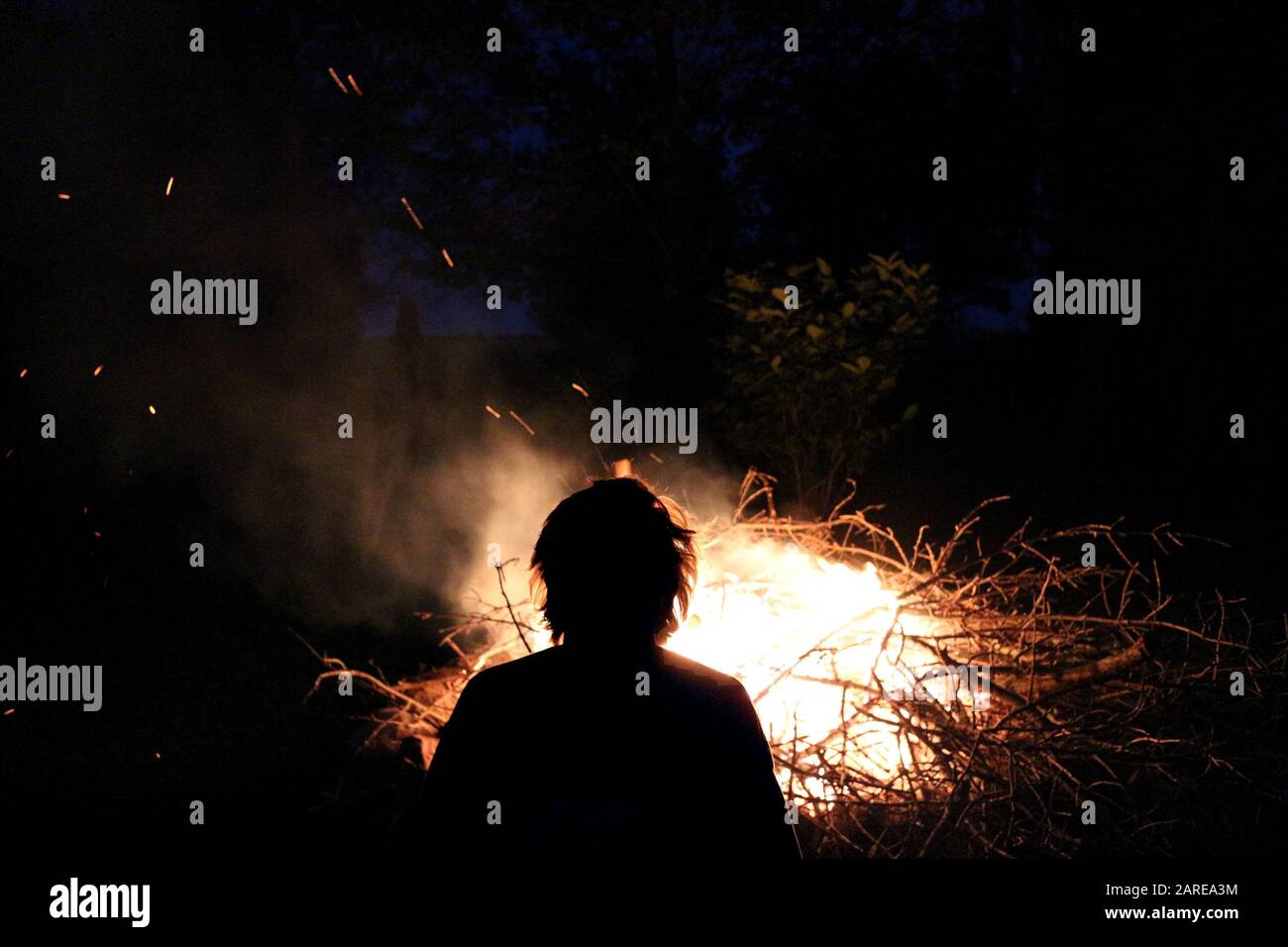 Silhouette Aufnahme eines Mannes, der in der Nähe des Lagerfeuers sitzt Ein Campingplatz Stockfoto
