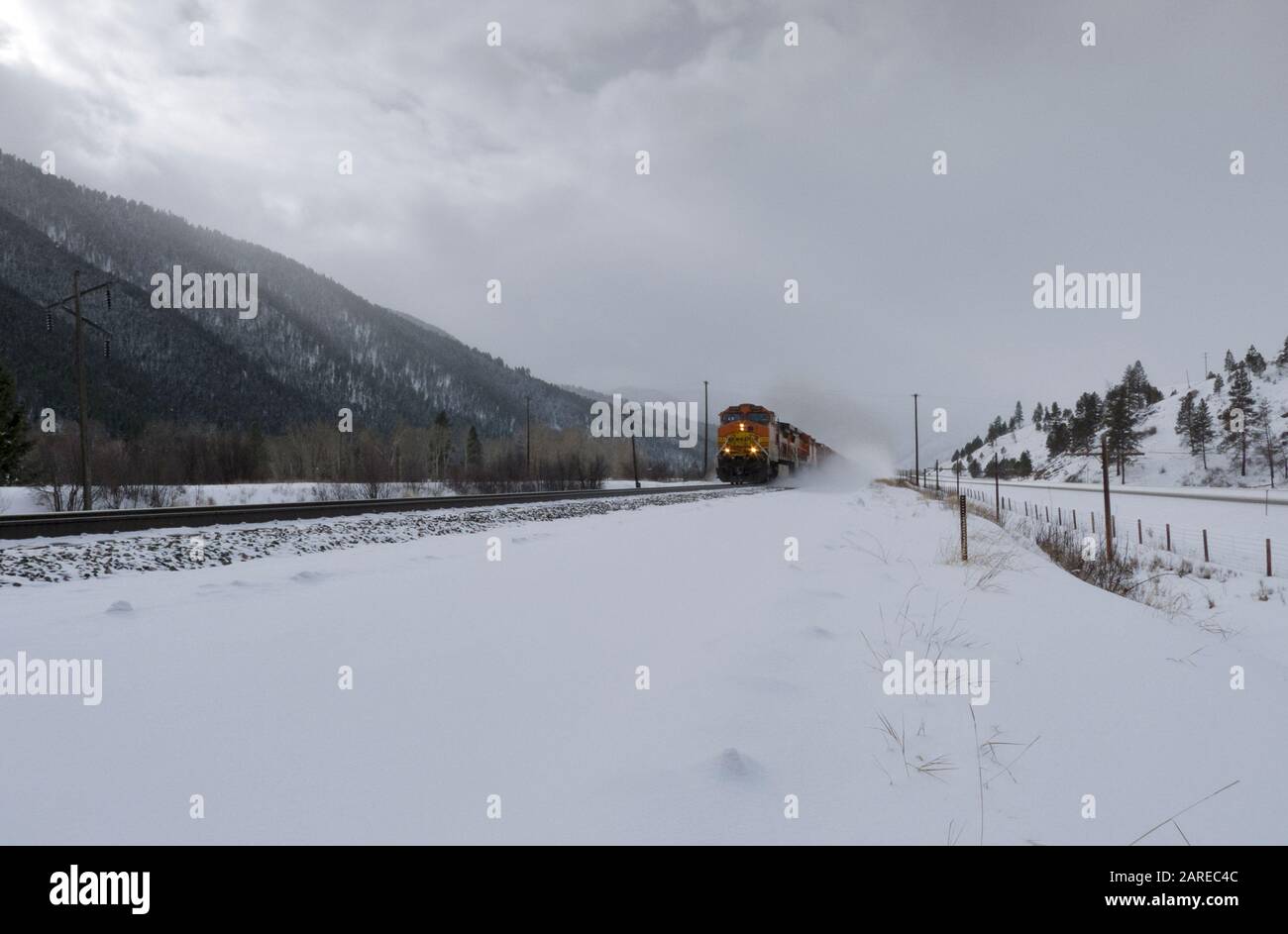 Ein BNSF-Zug, der an einem kalten, hellen, sonnigen Tag in Beavertail, Montana, die Gleise im Schnee hinunterfährt Stockfoto